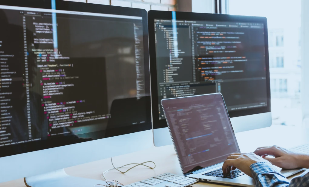 Laptop and two monitors with code on them